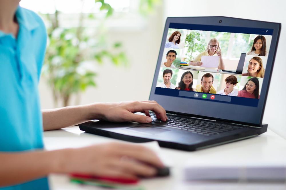 A picture of a boy in a blue shirt attending a virtual meeting on a grey laptop.